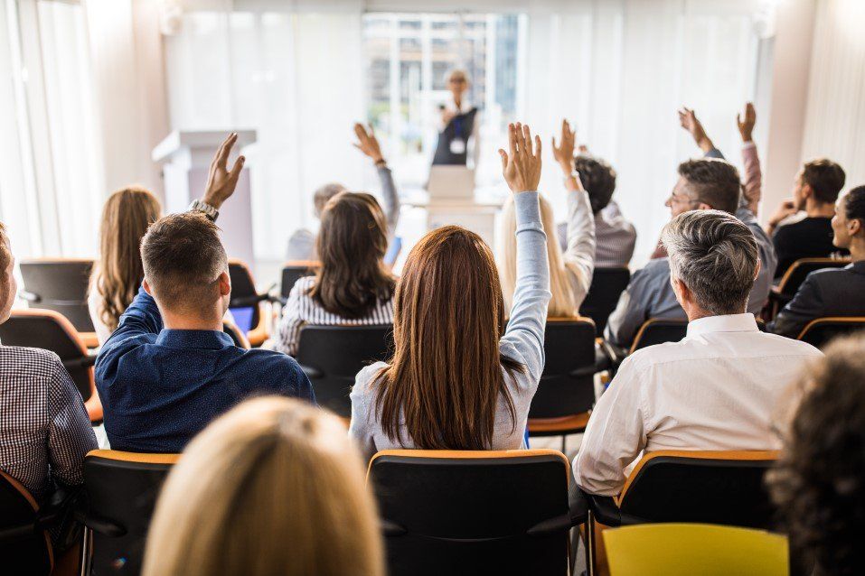 A group of people are sitting in a lecture hall with their hands up.