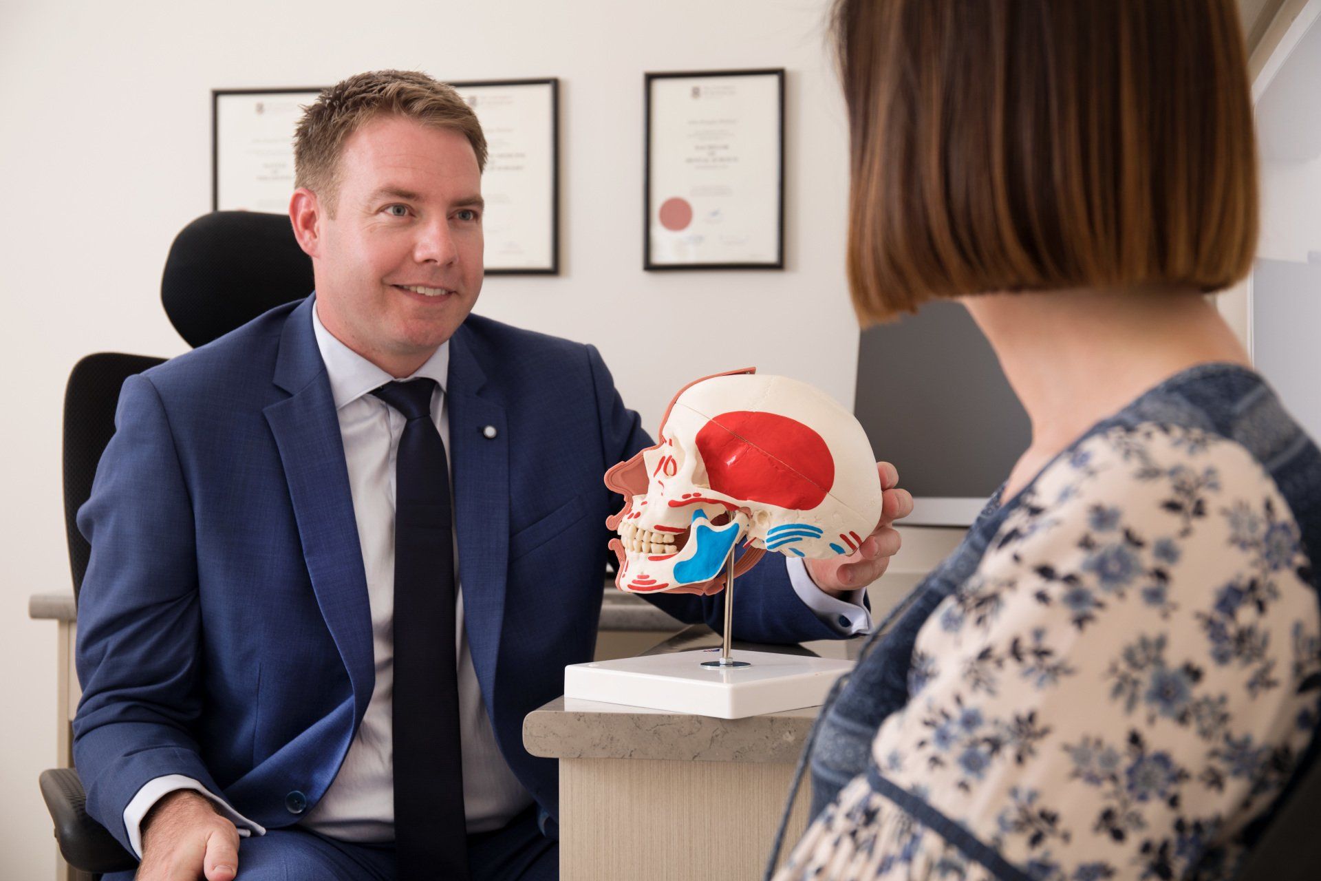 A man in a suit and tie is holding a model of a skull while talking to a woman.