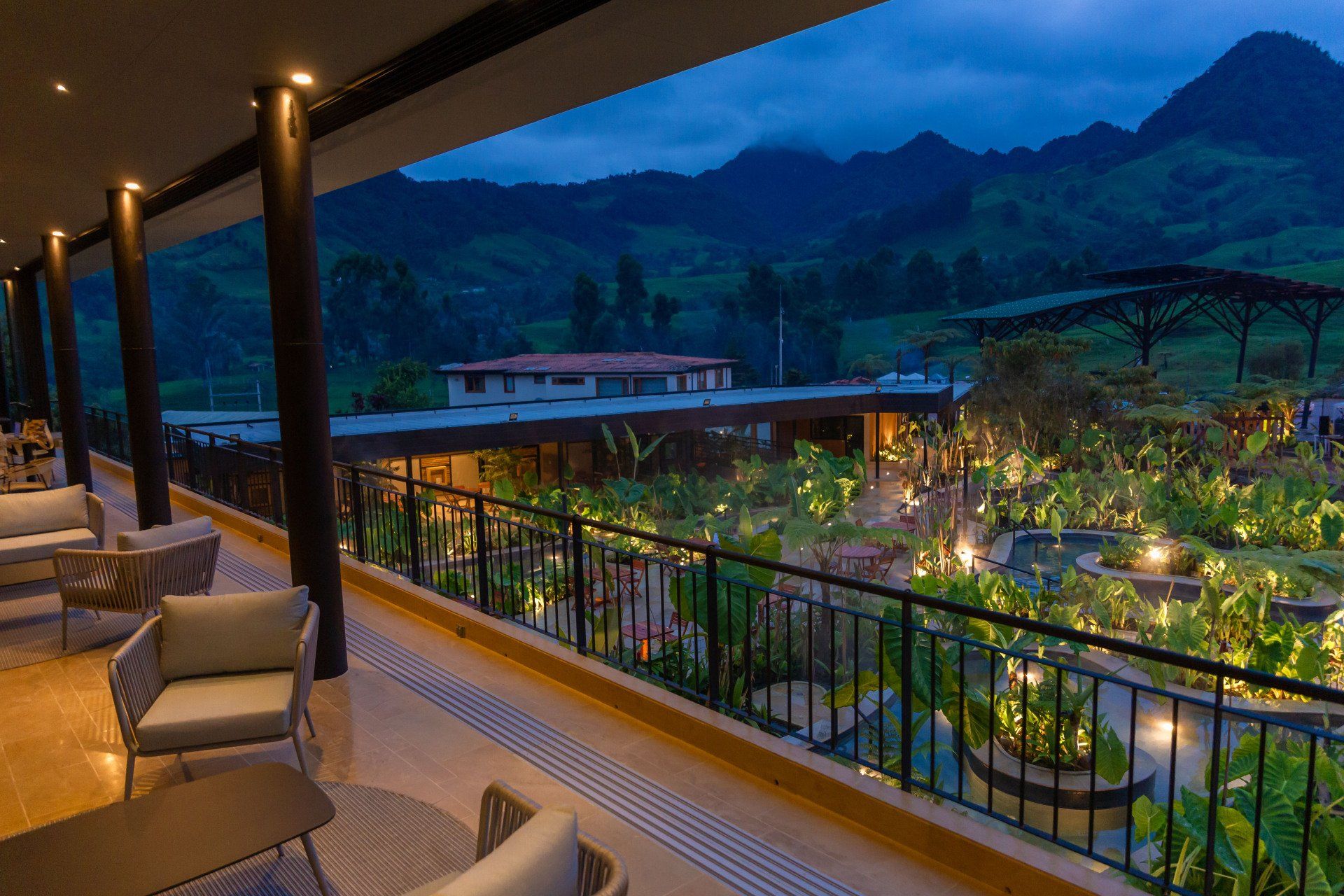 Restaurant terrace at Termales El Otoño, featuring tables, lounge chairs, and a nighttime view of the hotel’s green areas.