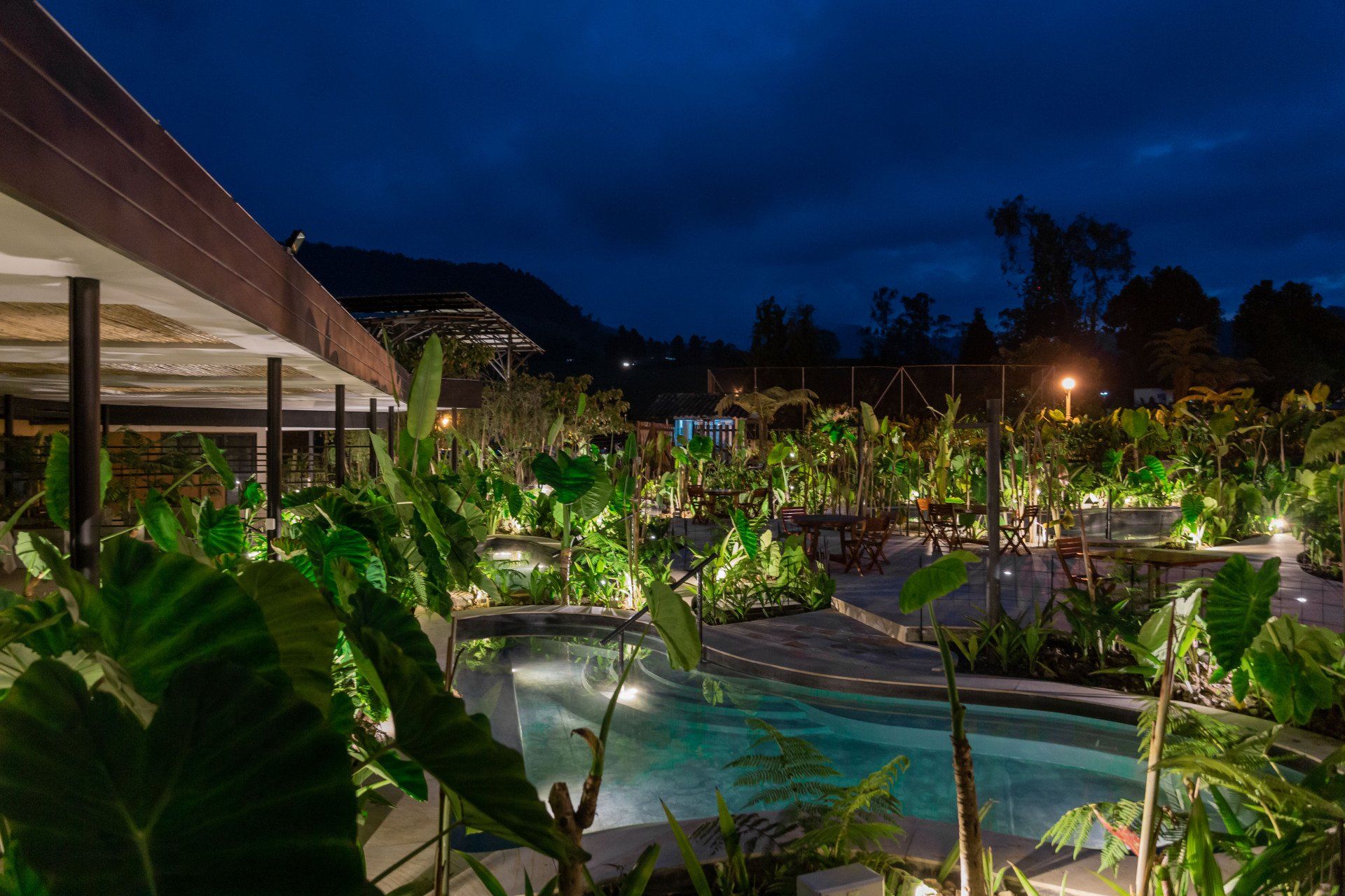 Night view of Termales El Otoño Hotel, featuring lit pathways, tropical gardens, and modern architecture.