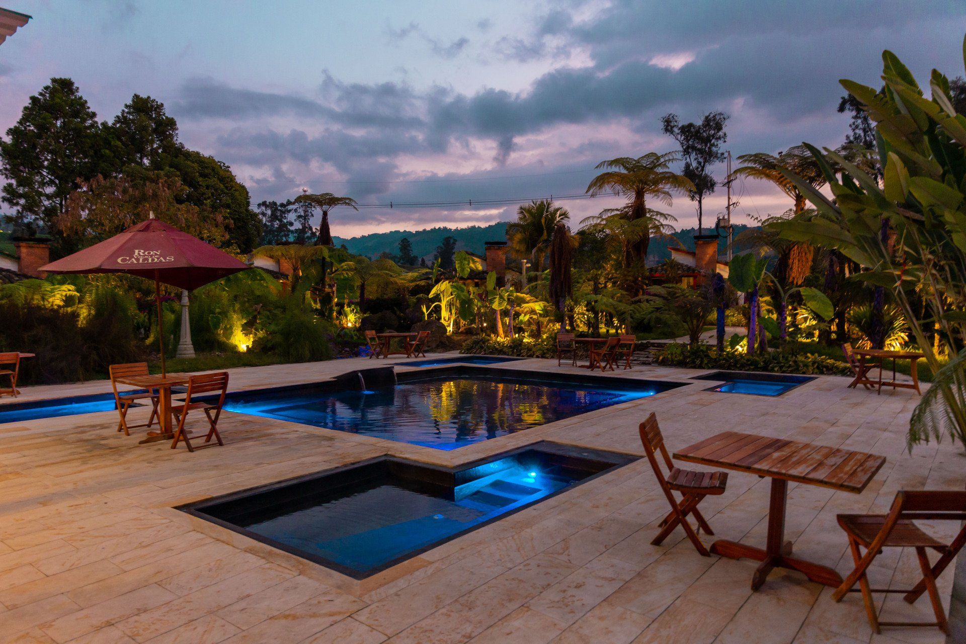 La Herradura pool at Termales El Otoño, featuring illuminated water pools, outdoor tables, and a nighttime atmosphere.