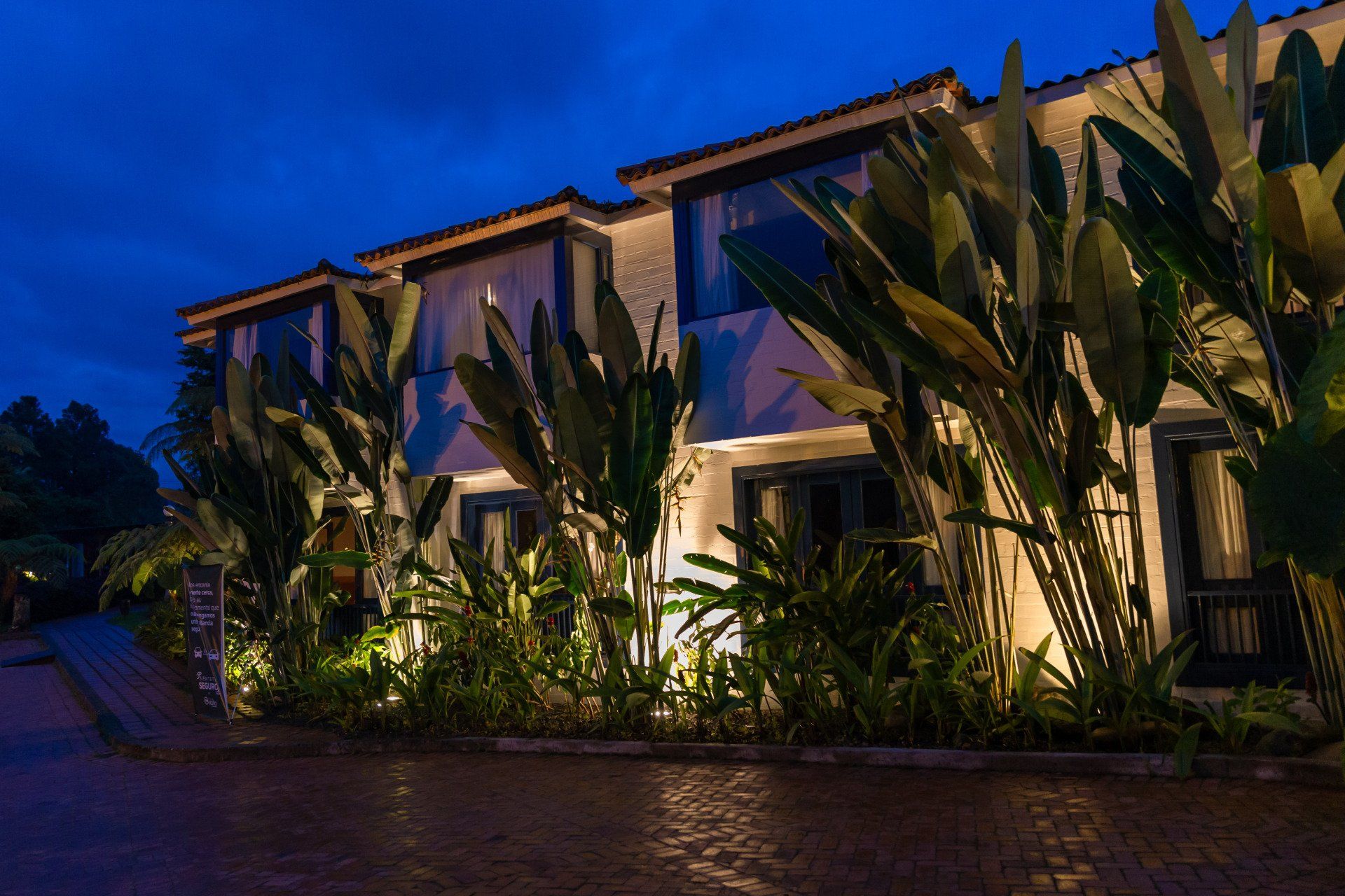 Outdoor areas at Termales El Otoño, featuring an illuminated facade, tropical gardens, and an entrance pathway at night.