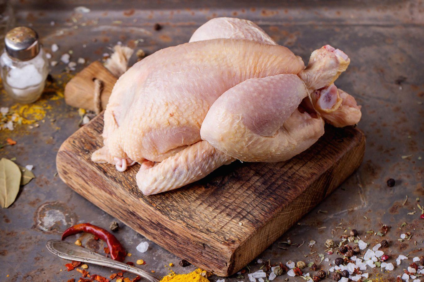 A raw chicken is sitting on a wooden cutting board.