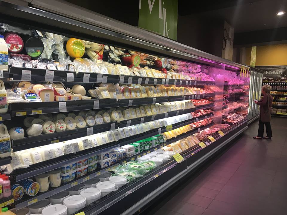 A woman is standing in front of a refrigerated section of a grocery store.