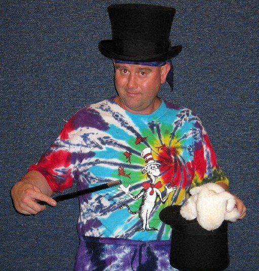 A man wearing a top hat and tie dye shirt is holding a top hat and a wand