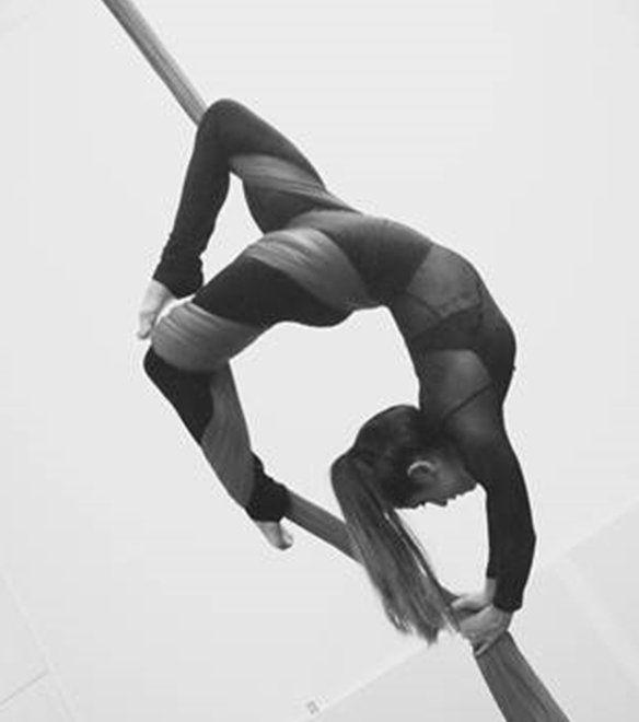 A woman is doing aerial acrobatics on a pole.