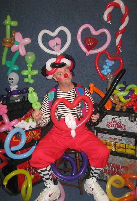 A clown is sitting on a stool surrounded by balloons