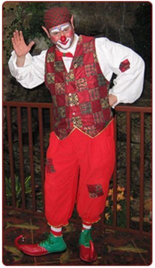 A man dressed as a clown is standing in front of a fence.