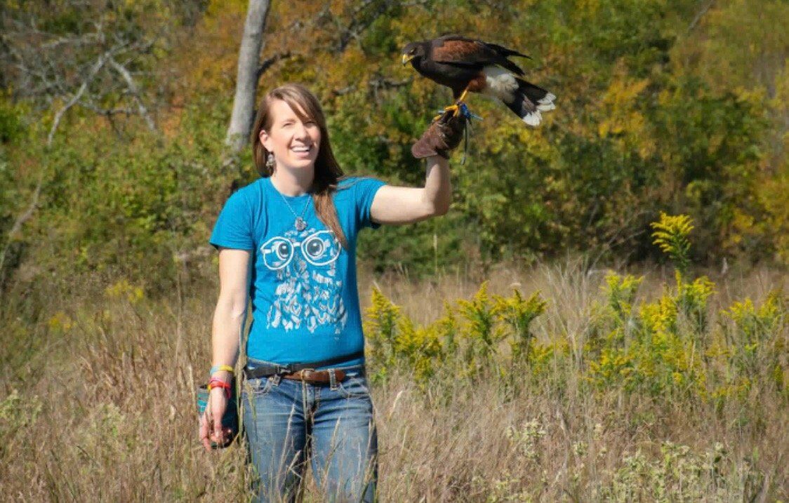 A woman is holding a bird in her hand in a field.