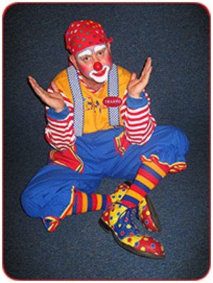 A clown is sitting on the floor with his arms outstretched