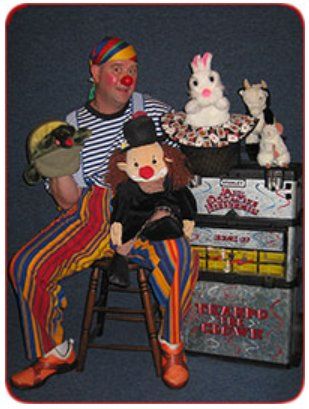A clown is sitting on a stool next to a stack of stuffed animals