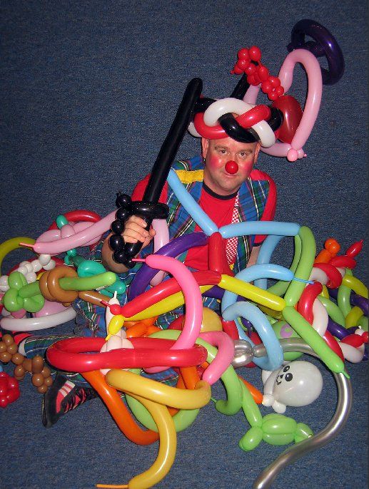 A man with a red nose is surrounded by balloons