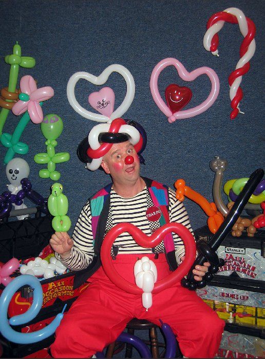 A clown is holding a heart shaped balloon in his hand