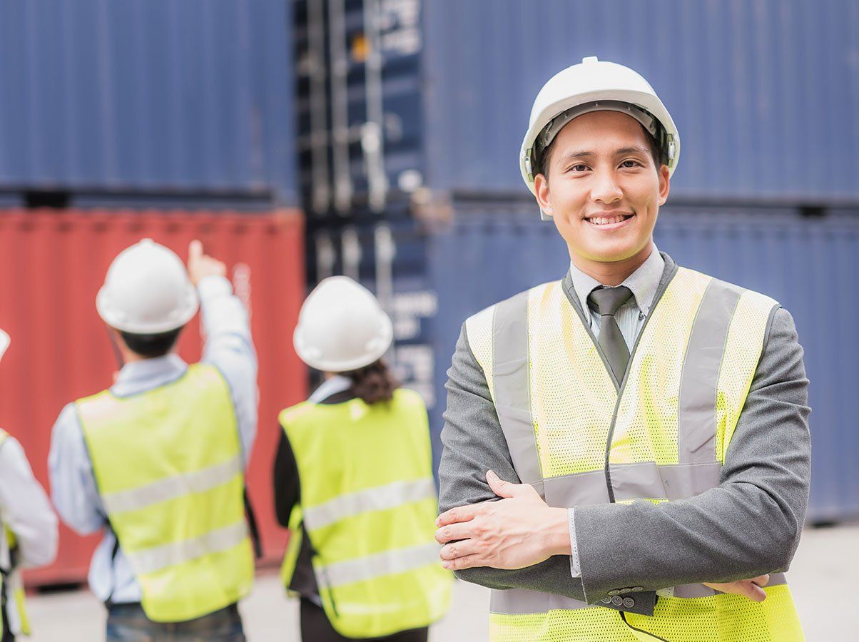 A man in a suit and hard hat is standing in front of a group of construction workers.