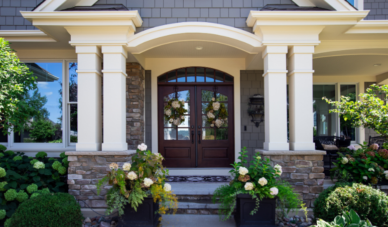 Front entrance of a house with stone columns, arched doorway, and potted flowers