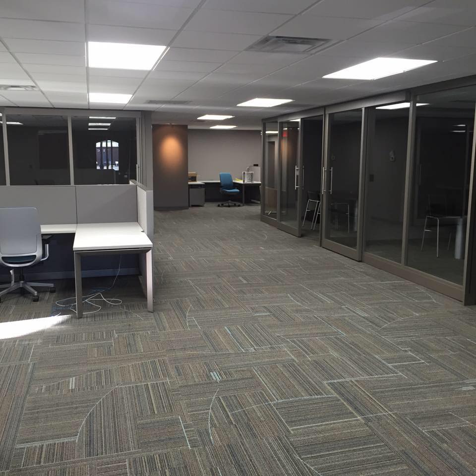 Empty office area with carpet, desks, and glass walls under bright ceiling lights