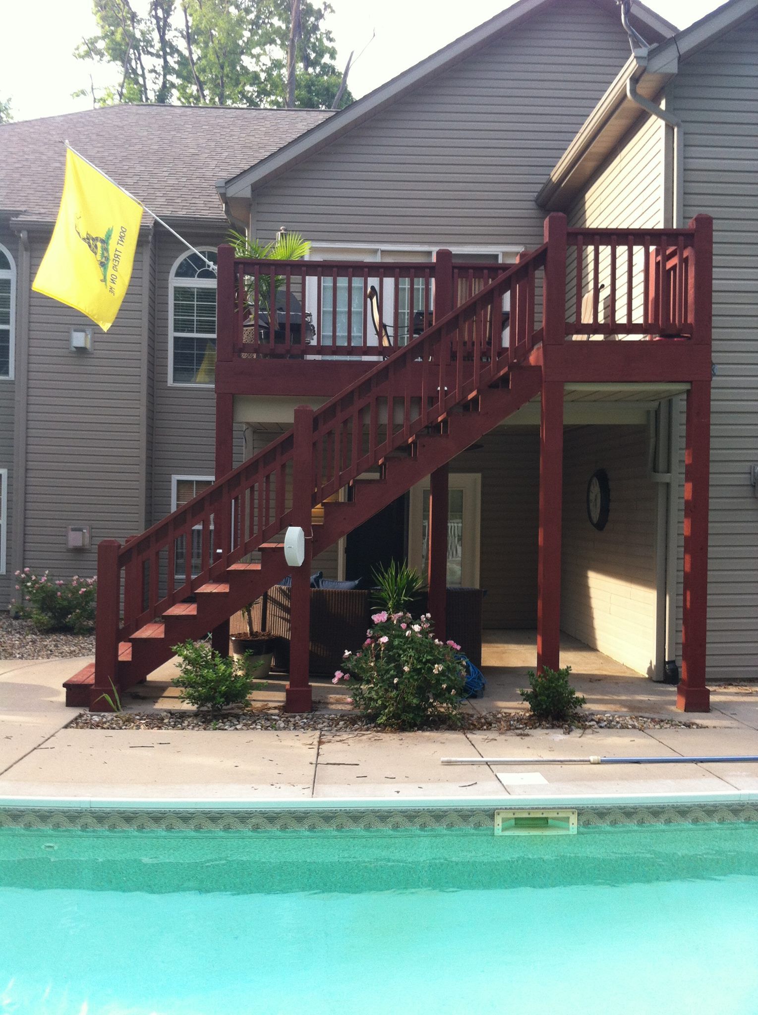 Backyard pool beside a raised wooden deck and stairs, with a yellow flag on the house.