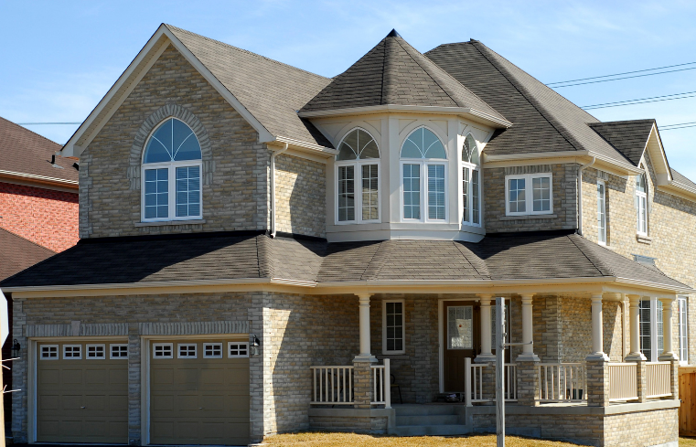 Two-story stone house with a front porch, bay window, and double garage under a gray roof