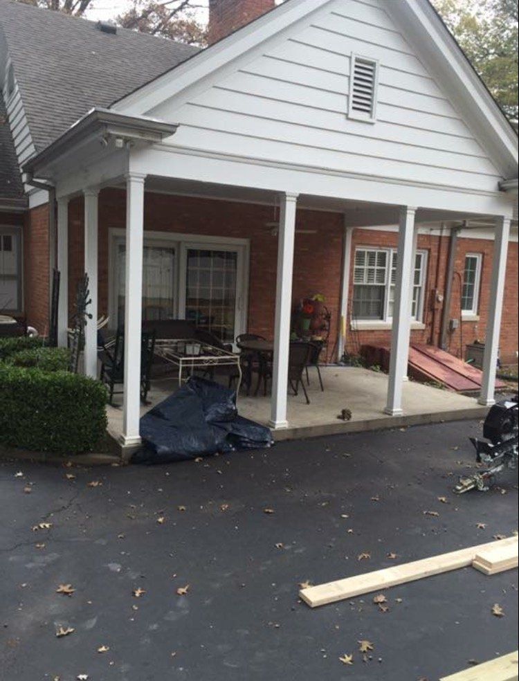 Front porch with white columns on a brick house, covered in part by a dark tarp and a wooden plank on the driveway
