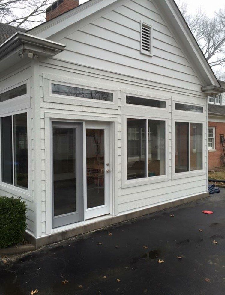 White house exterior with large front windows and a glass door beside a wet driveway
