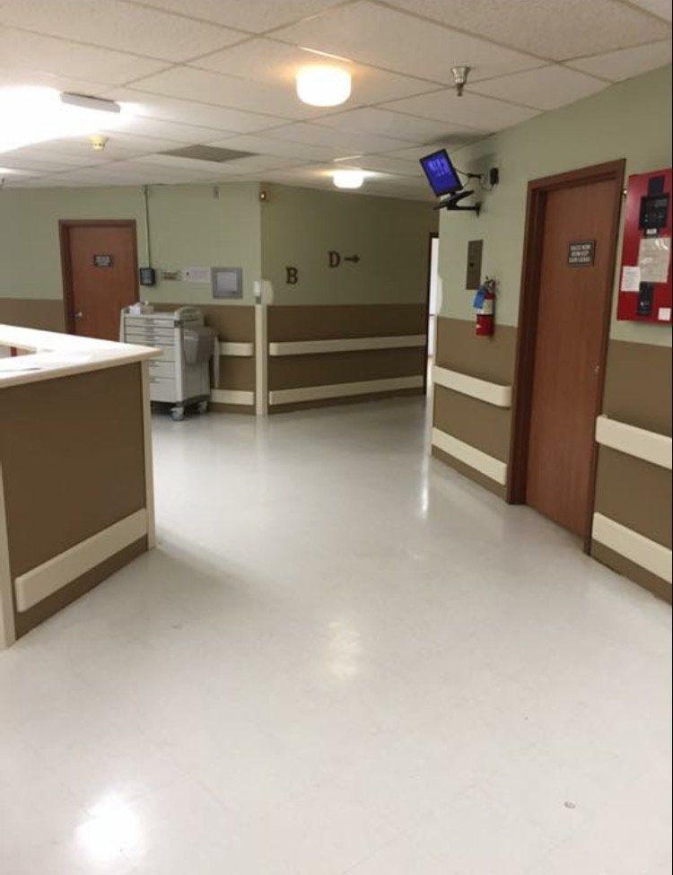 Empty hospital hallway with beige walls, brown doors, and a wall-mounted TV.