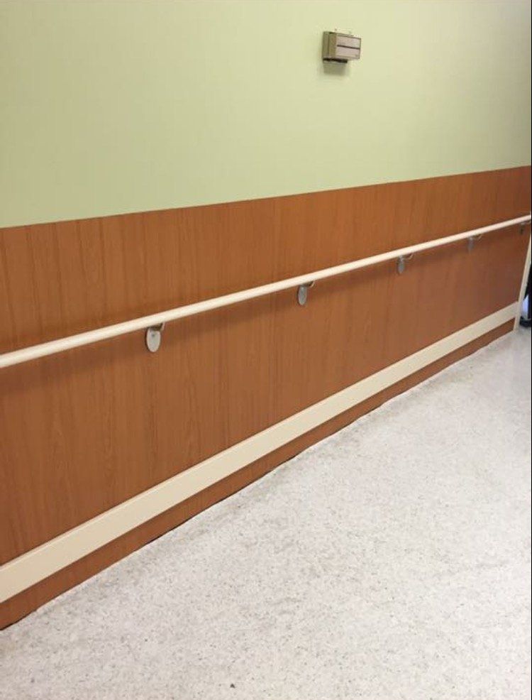 Empty hallway with a wooden handrail and green wall above a speckled floor.