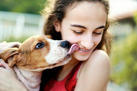 A young girl is holding a dog in her arms and the dog is licking her face.