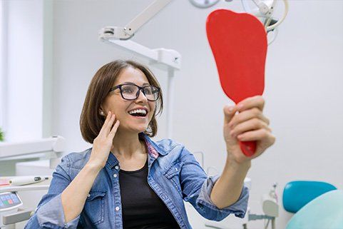 A woman is looking at her teeth in a dental mirror.