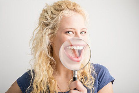 A woman is looking through a magnifying glass at her teeth.
