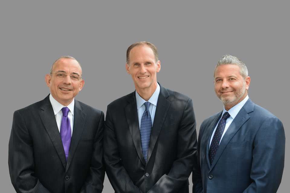 Three men in suits standing together; gray background.