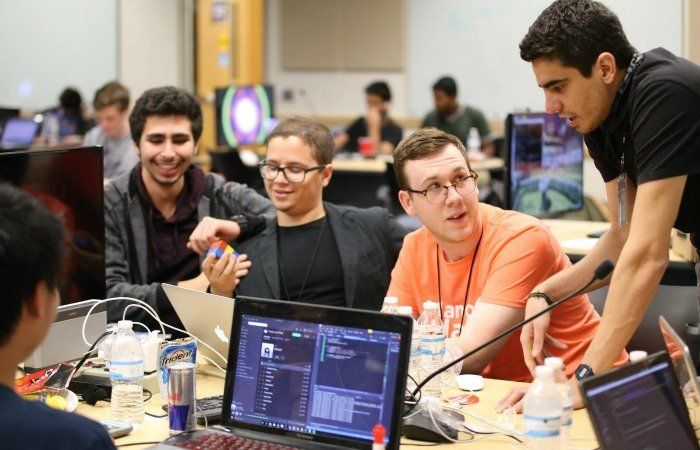 A group of young men are sitting around a table with laptops.