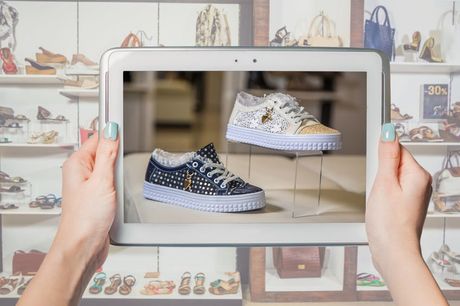 Hands holding a tablet displaying black-and-white sneakers in a shoe store display