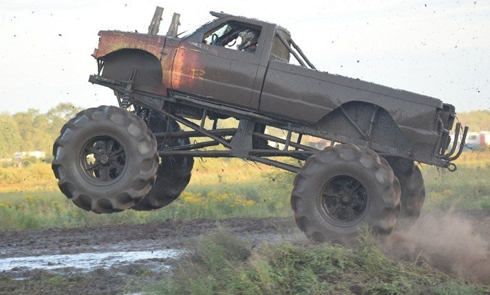 Lifted gray off-road truck airborne over a dirt track, kicking up dust