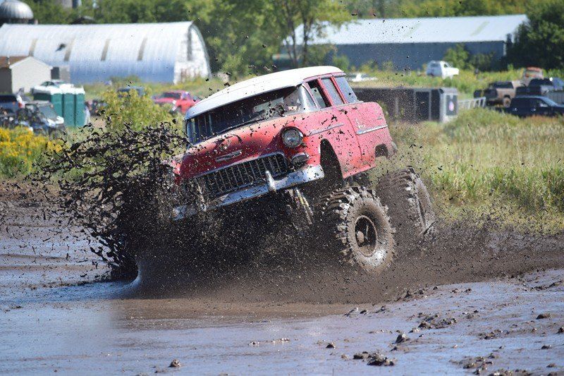 Red off-road truck splashing through mud on a wet track near farm buildings