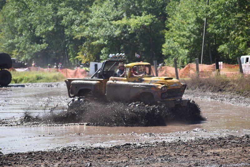 Yellow off-road truck splashing through a muddy track in a wooded outdoor area