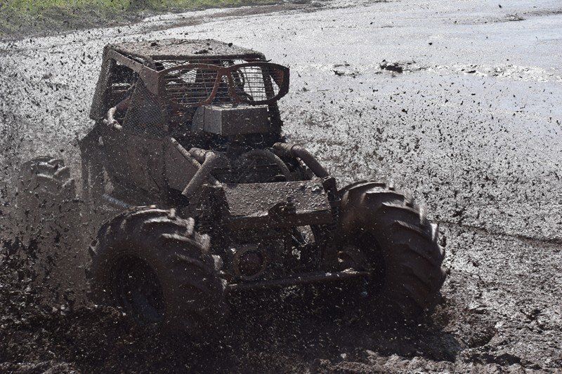 Mud-covered off-road buggy driving through a muddy puddle at speed.