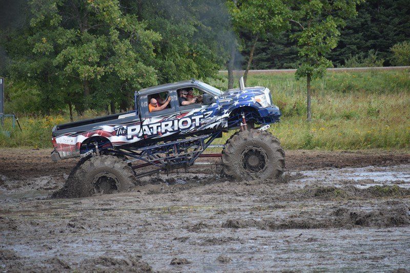 Blue mud-covered off-road truck with PATRIOT lettering splashing through a muddy field