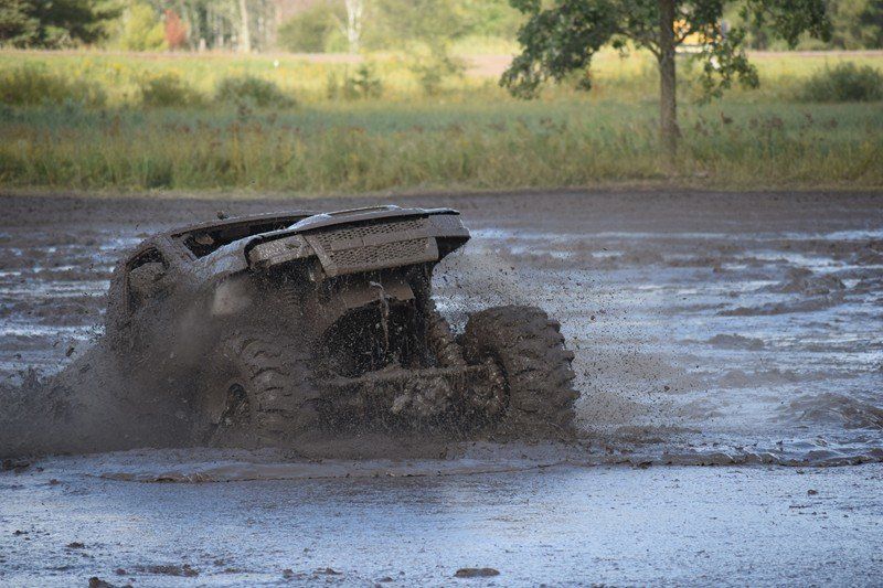 ATV splashing through muddy water in a shallow field, with grass and trees in the background
