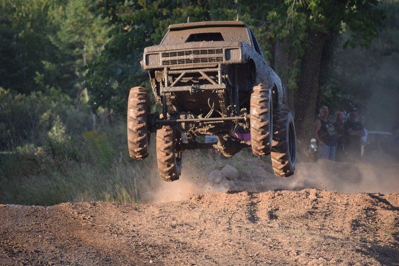 Off-road truck jumping over a dirt mound on a dusty forest trail