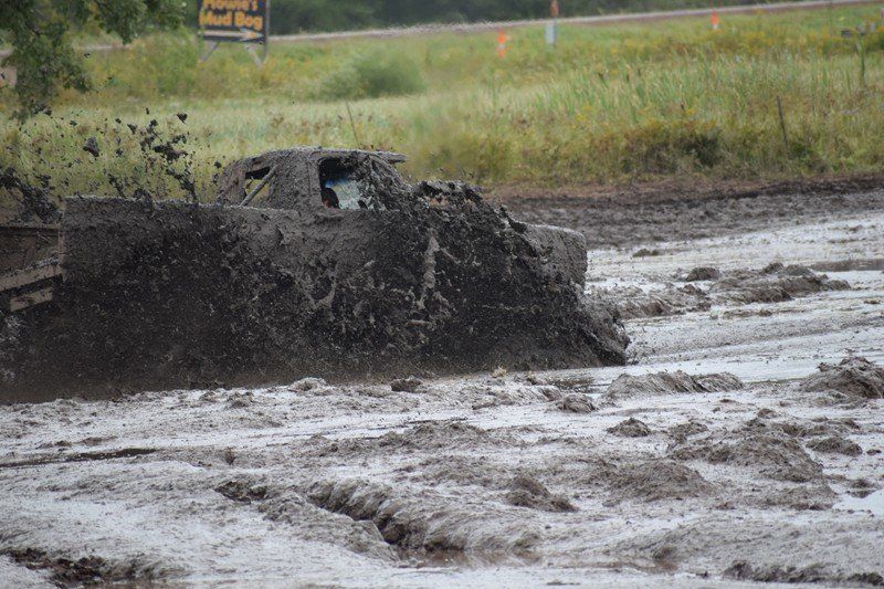 Mud-covered off-road vehicle splashing through a muddy track near grassy roadside.