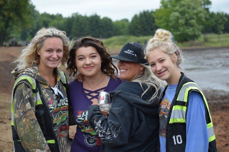 Four smiling people outdoors, two in reflective safety vests, standing together in a field.