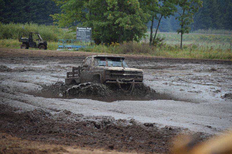 Pickup truck splashing through a muddy off-road track near a wooded field