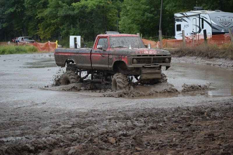 Red pickup truck splashing through deep mud at a muddy off-road site