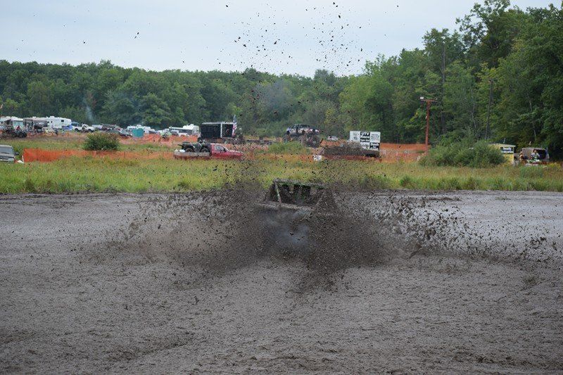 Off-road truck splashes through a muddy puddle, sending water and dirt high into the air.