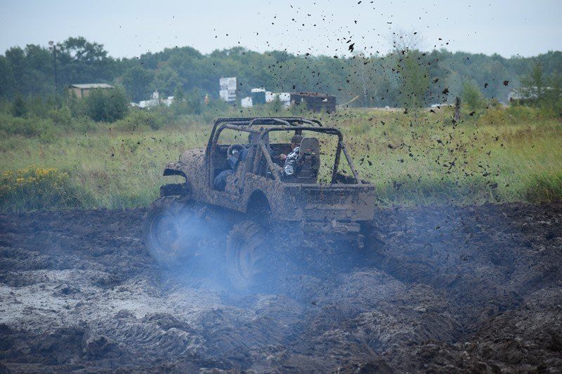 Off-road buggy splashing through muddy water on a dirt track, with mud spraying into the air.