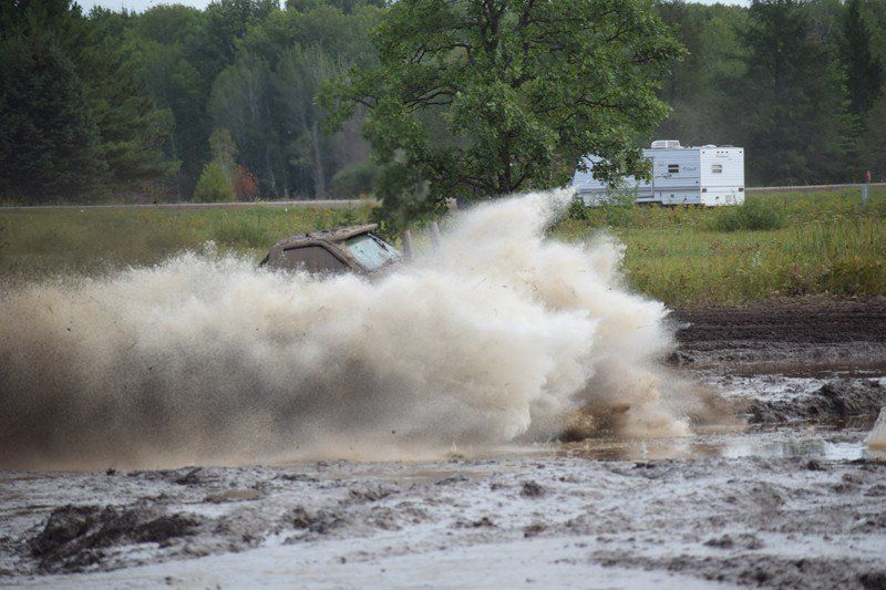 Truck splashes through muddy water, creating a large spray in a rural off-road area