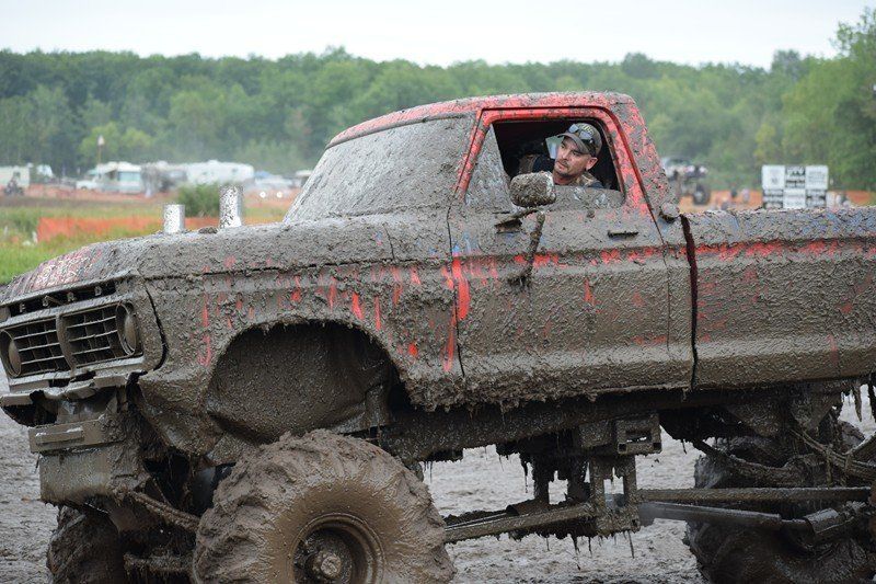 Muddy lifted pickup truck with a driver inside at a muddy off-road track