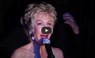 Singer at a microphone on a dark stage, with a video play icon over the image