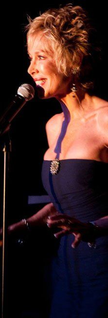 Singer in a dark blue strapless dress performing into a microphone on stage.