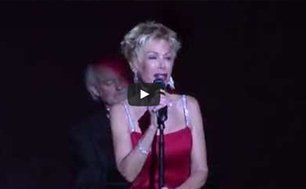 Singer in a red dress performing into a microphone on a dark stage
